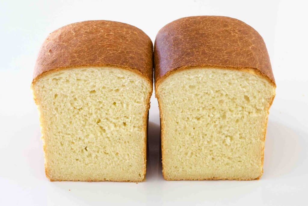 a loaf of soft sandwich bread on a white background; the loaf has been cut in half and turned to the camera to show the interior.